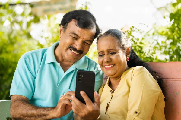 在公园边看手机边笑着的印度老年夫妇 社交媒体 科技和退休生活方式的概念 — 图库照片