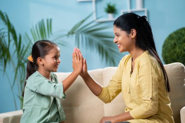 Çocuğa odaklan, evde kanepede otururken kızıyla oynayan mutlu Hintli anne - aile zamanı, hafta sonu tatilleri ve neşeli çocukluk kavramı.
