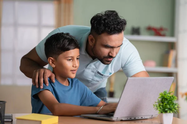 Indian father explaining or teaching from laptop to son at home - concept of family support, home education and Homework assistance.
