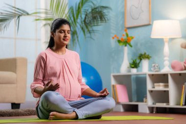 Nilüferli Hintli barışçıl hamile kadın yoga minderleri üzerinde meditasyon yapıyor. Hamilelik sırasında farkındalık, rahatlama ve kendine bakım kavramı..