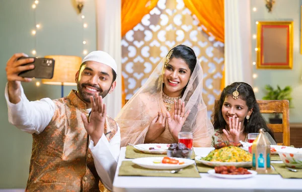 Happy smiling indian muslim family on video call on mobile phone during ramadan festival dinner or feast at home - conecept of distant relationship, festival celebration and cyberspace