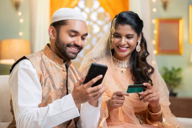 Hintli mutlu müslüman çift alışveriş için internet üzerinden alışveriş yapıyor. Ramazan festivali satışları sırasında cep telefonuyla alışveriş yapıyor. İlişki, teknoloji ve e-ticaret kavramı.