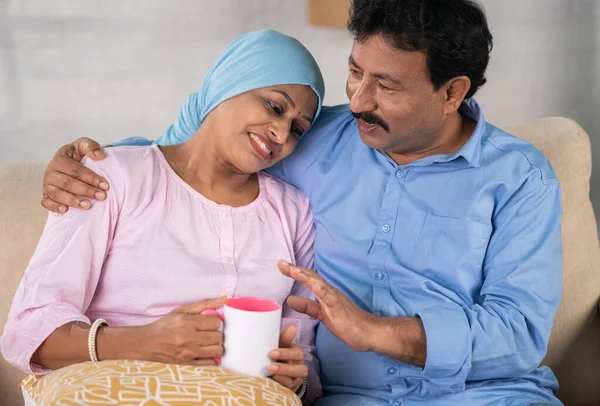 Happy smiling indian cancer woman with husband talking spending time by embracing at home - concept of rehabilitation, communication and family togetherness