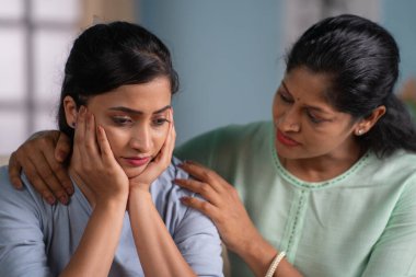 Hintli anne üzgün ve endişeli kızını evde teselli ediyor. Aile desteği, annelik ve koşulsuz sevgi kavramı..