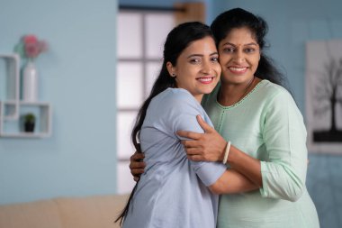 Mutlu, gülümseyen Hintli yetişkin bir kız çocuğu, kameraya bakarak annesine sarılıyor. Aile bağı, birliktelik ve annelik kavramı..