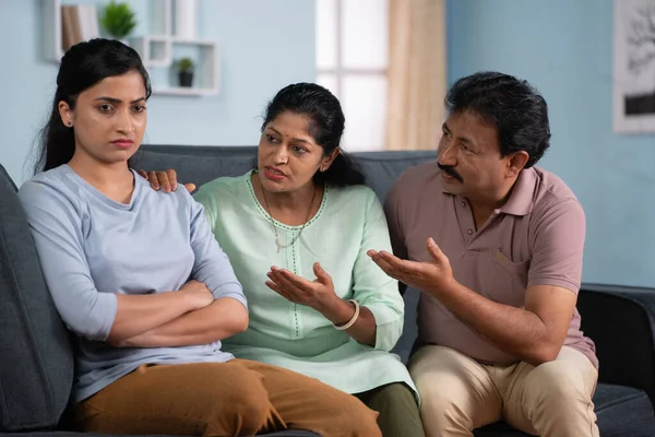 focus on parents, Indian parents consoling to sad or angry daughter after quarrel while sitting on sofa at home - concept of family bonding, Emotional Support and Parental Comfort.