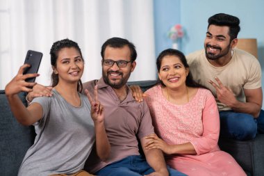 Neşeli Hintli orta yaşlı ebeveynler ve kardeşleri evde cep telefonlarıyla selfie çekiyorlar. Aile birliği, teknoloji birleşmesi ve Mutlu Toplantılar kavramı..