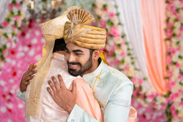 happy Indian son as groom hugging his father during Marriage or wedding ceremony on stage - concept of fatherhood, relationship Bonding and marriage moments.