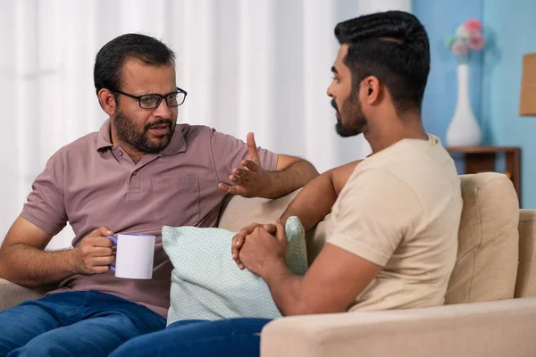 Serious indian father discussing with son while having coffee at home - concept of Parental Advice, family Mentorship and sharing Life Lessons.