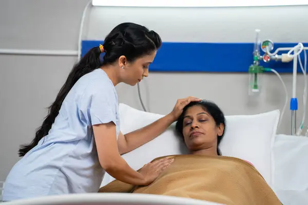 Indian daughter feeling bad or worried for sick sleeping mother at hospital ward- concept of family caring, medical treatment and relationship bonding.