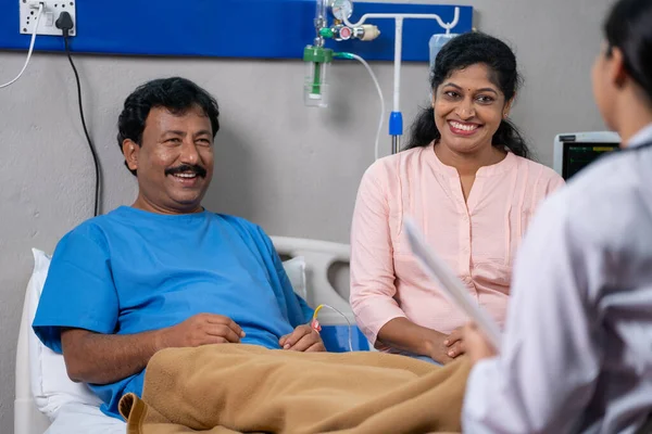 Shoulder shot of friendly indian doctor talking with recovered patient and wife at hospital - concept of successful treatment, medicare support and Conversation.