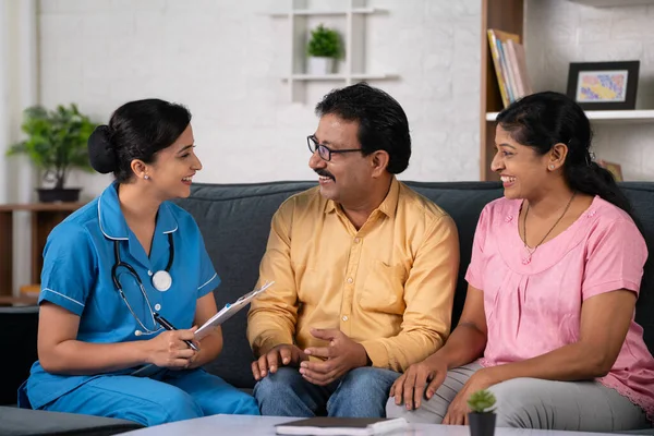 Indian nurse happy about patient recovery during home visit while talking with couple - concept of successful treatment, Health Progress and Caring Interaction.