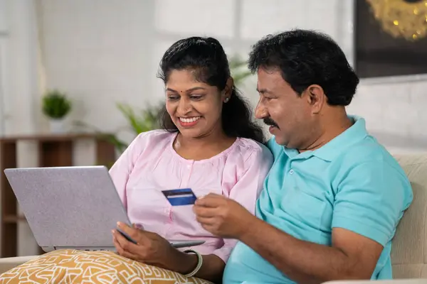 Happy indian middle aged couple making online payment using credit card on laptop at home - concept of online shopping, relationship bonding and Secure Payment.