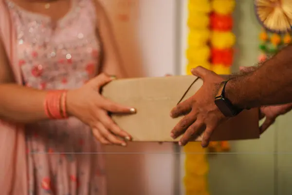 Focus on hand, close up shot of girl hands receiving parcel box from delivery boy during festival Diwali sales or celebration at home - concept of online shopping, ecommerce purchase and instant