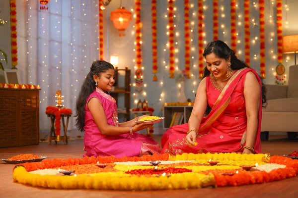 focus on kid,Happy Indian young Mother with daughter preparing Diwali rangoli for celebration - concept of home decoration, family bonding and religious custom