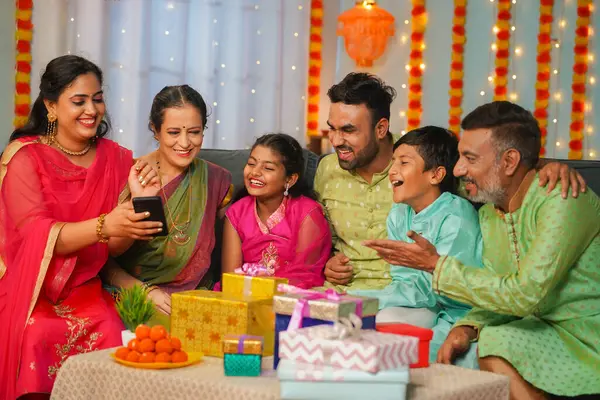 Group of happy indian joint family seeing mobile phone during family diwali festival celebration - concept of emotional reunions, Relationship bonding and social media sharing.