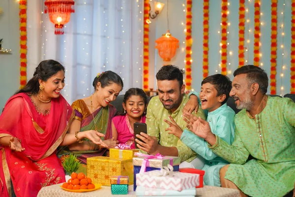 Group of happy indian joint family seeing mobile phone during family diwali festival celebration - concept of emotional reunions, Relationship bonding and social media sharing.