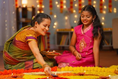 Mutlu büyükanne ve kız torun çiçek rangoli üzerine diya lambaları yerleştiriyor - diwali festivali hazırlığı, gelenek ya da gelenek ve nesiller konsepti.