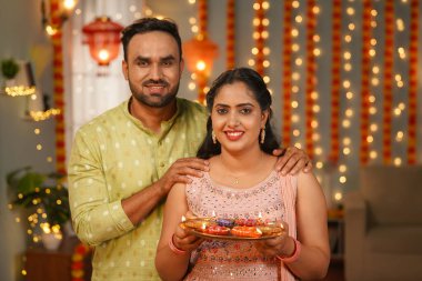 Mutlu gülümseyen genç çiftlerin portresi. Evde Diwali kutlamaları sırasında kameraya bakıyorlar. Maneviyat, adanmışlık ve şenlik anları..