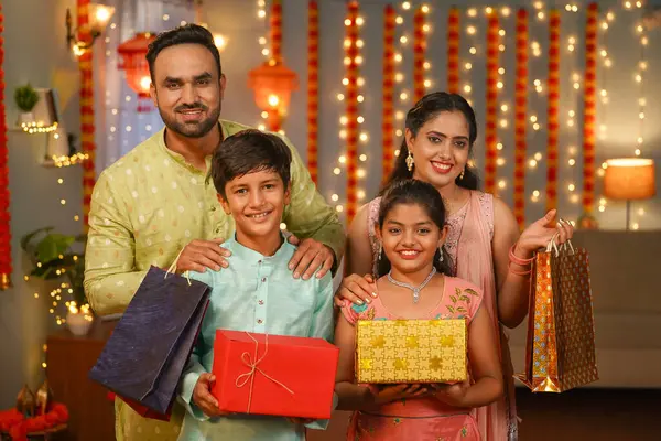 Happy Indian family standing with gift boxes and Shopping bags by looking camera during diwali celebration at home - concept of festive shopping, sales and offers.