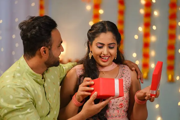 Happy husband giving diwali gift or present to wife at home during festival celebration at home - concept of special occasion, gratitude and family bonding.