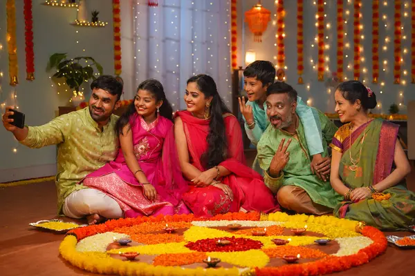 Group of Indian joint family members taking selife in front of decorated diwali rangoli at home - concept of festival gathering, reunion and festival celebration.