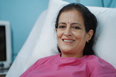 Mutlu gülümseyen bir kadının portre çekimi başarılı bir tedaviden sonra hastane yatağında kameraya bakarken çekildi. Umut, memnuniyet ve sağlık kavramı..