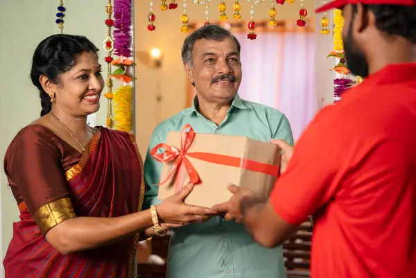 Elderly senior couple receiving ordered online delivery box from delivery person - concept of diwali festive gifting, ecommerce shopping and sales or discounts shopping