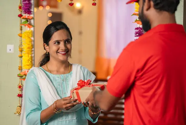Happy excited indian girl receiving box from delivery person during diwali festive gifting - concept of online or ecommerce shopping, doorstep delivery and special occasion
