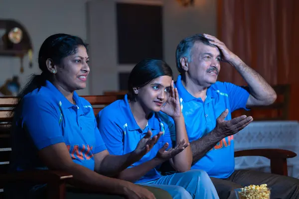 Side view of family got sad due to loss of cricket match while watching on tv or television at home - concept of competition, championship and disappointment audience or fans