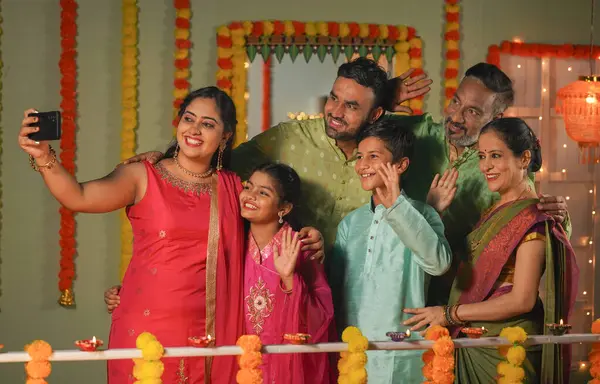 Group of Indian family members making video call on mobile phone for diwali wishes or greetings during festive celebration at home - concept of holiday gathering, traditional culture and communication