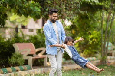 Babaya odaklan, neşeli Hintli baba küçük kızını parkta döndürerek oyna. Beraberlik kavramı, hafta sonu tatilleri ve aile zamanı..