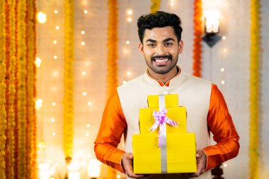 Geleneksel etnik kıyafetli mutlu Hintli adam evde kameraya bakarak hediye kutusuyla - diwali kutlaması, festival teklifleri ve reklam konsepti.