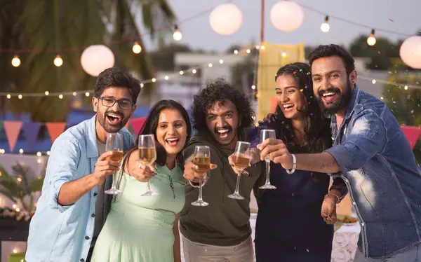 Group of youthful Friends saying happy new year by holding champagne glassless during 2024 party celebration - concept of friendship, nightlife and evening gathering.