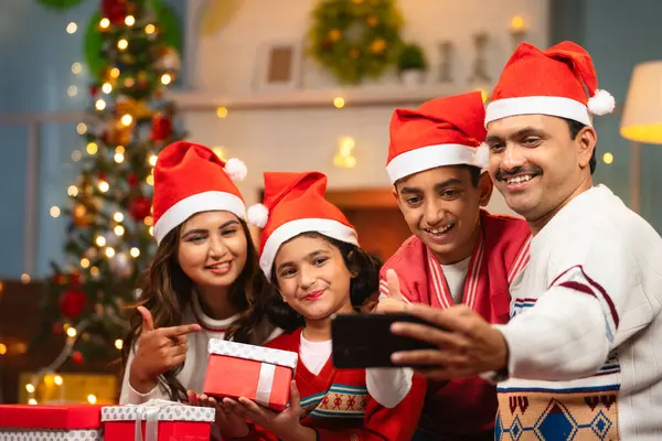 focus on boy kid,Happy indian family taking selife on mobile phone with gifts in hands during charismas holiday celebration - concept of family bonding, social media sharing and festive gathering