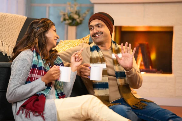 Relaxed Indian couple in winter wear spending time together by drinking tea or coffee at home - concept of romantic weekend, family bonding and holidays.