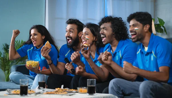Group of excited Indian cricket fans celebrating by shouting for Team India win in cricket while watching tv at home - concept of cheering supporters, entertainment and championship match.