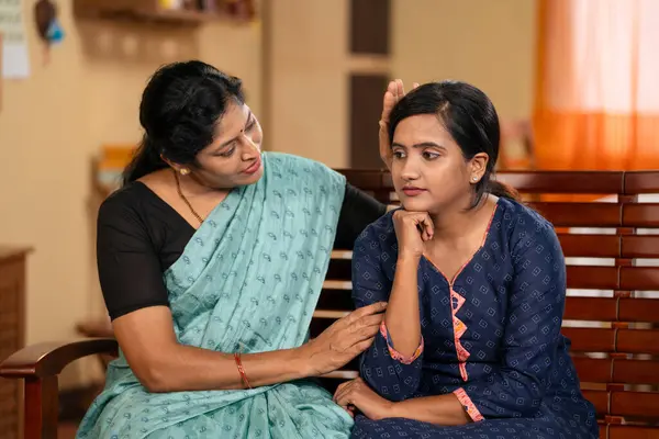 Indian middle aged mother consoling worried daughter at home - concept of parental care, family support and concern or compassion.