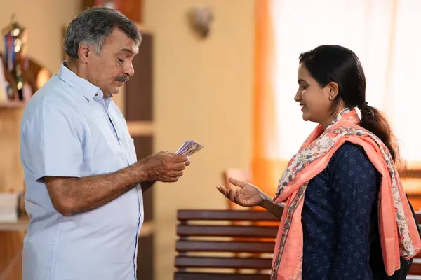 Indian middle class father giving pocket money to college going daughter at home - concept of education support, financial assistance and responsibility.