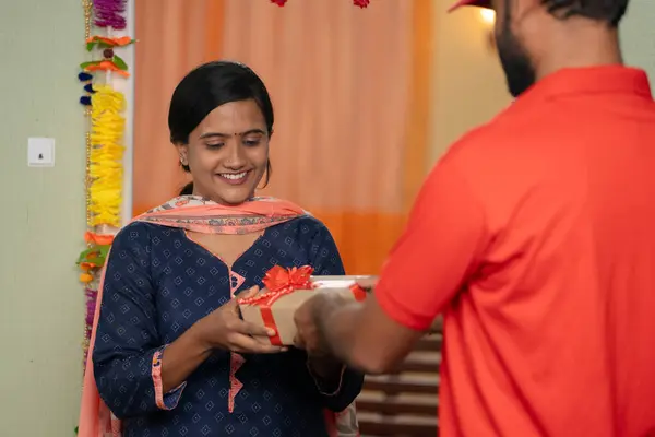 Happy young girl receiving parcel or gift box from delivery person at home - concept of door step fast delivery, ecommerce shopping and online order