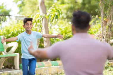 Çocuğa odaklan, neşeli Hintli oğlanın parkta babaya sarılmaya ya da kucaklaşmaya geldiği omuz atışı - aile bağı, mutlu kavuşma ve aile bağı kavramı.