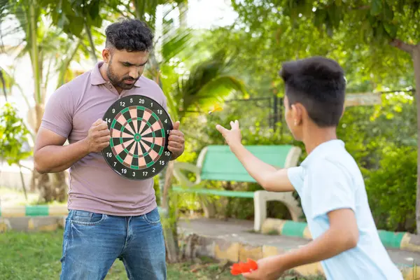 Indiaanse Zoon Gooien Magnetische Dart Dartbord Terwijl Vrolijke Vader Houdt Stockafbeelding