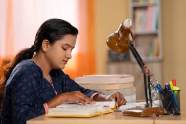 Hintli genç kızın evde okuyarak devlet veya kamu sınavına hazırlanırken yan görüntüsü - konsantrasyon, eğitim ve hevesli kız