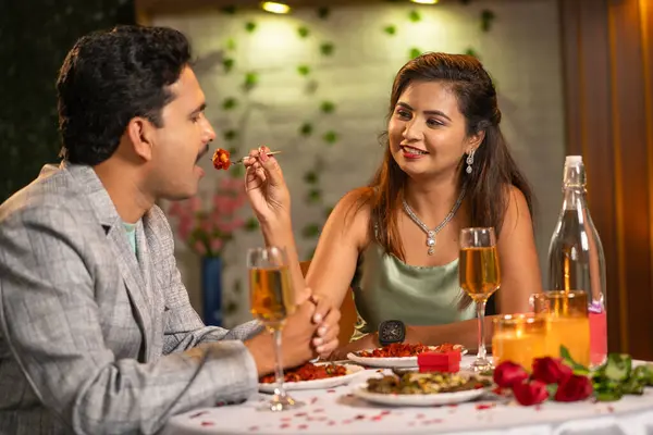 Romantic woman feeding his husband by giving bite during candlelight dinner - concept of romantic date night during valentines day and special occasion.