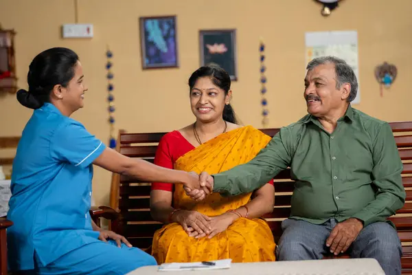 happy Indian nurse or caretaker greeting senior elderly couple at home during routine health check up - concept of professional occupation, medical consultation and diagnosis.