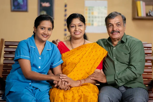 Happy indian nurse with elderly couples during home health checkup looking at camera - concept of family bonding, proud parents and professional occupation.