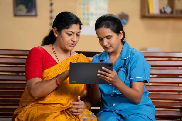 Indian nurse or caregiver at home explaining to middle aged woman or patient at home during home consultation - concept of medical counselling, professional occupation and healthcare service.