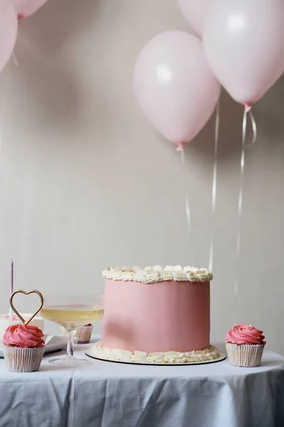 Big beautiful pink cake with cupcakes and white wine on the table on a white background. Birthday celebration. Pink balls on a white background. Birthday concept