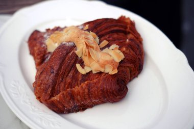 Çok lezzetli bademli kruvasan. Beyaz bir tabakta badem yapraklarıyla süslenmiş yumuşak hamur işlerinden yapılmış.