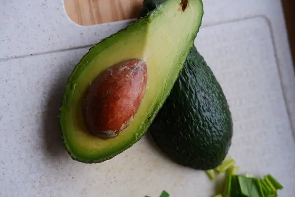 green ripe avocado cut in half and fresh wild garlic leaves lie on the kitchen board. ripe and juicy avocado. wholesome and healthy eating. green healthy vegetables close-up